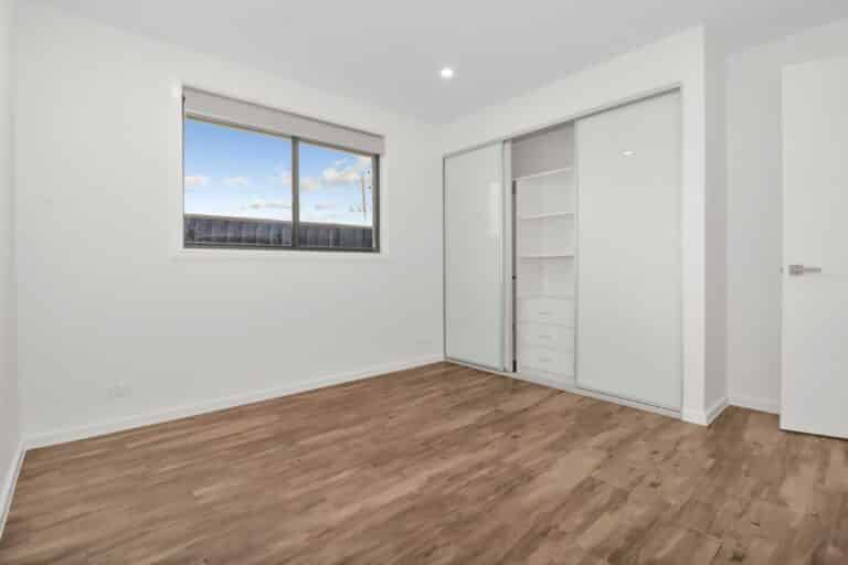 Empty room with wooden floor, white walls, large window, and built-in closet with sliding glass doors and drawers inside.