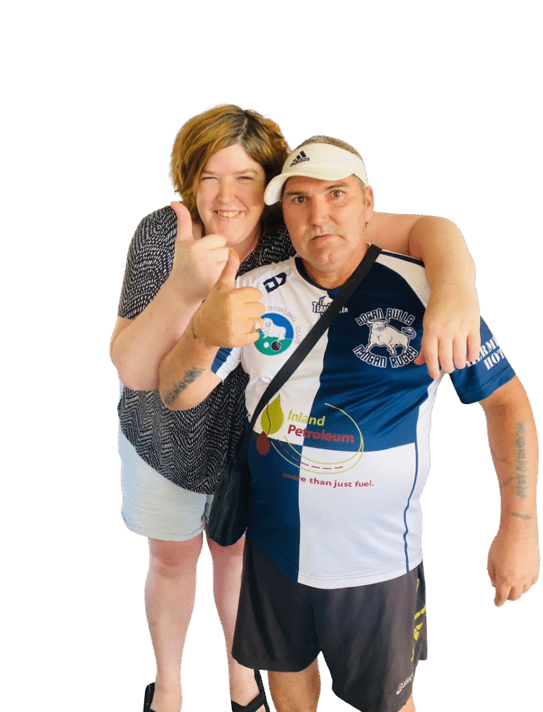 A woman stands with her arm around a man’s shoulders, both facing the camera. The man wears a sports shirt and visor, and both are giving a thumbs-up gesture.