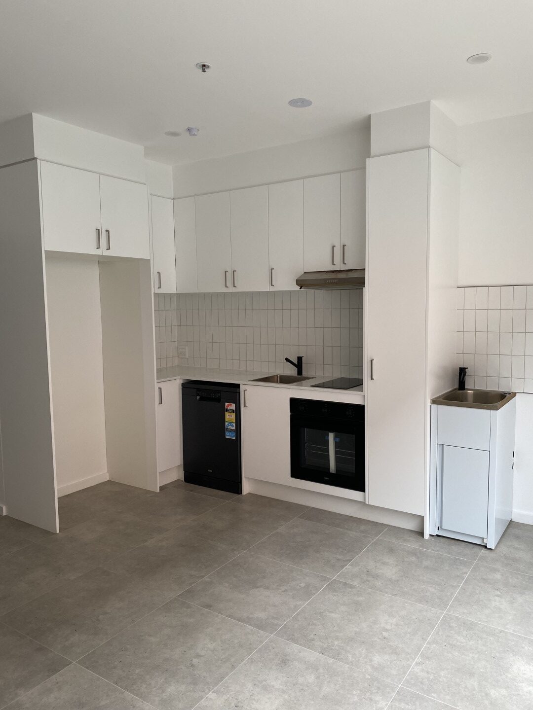 Modern kitchen with white cabinets, an oven, stove, dishwasher, stainless steel sink, tiled backsplash, and a small laundry area with a washing machine on the right.