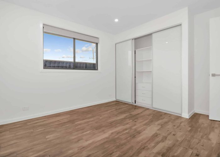 CHESTERHILL 2 2 An empty room with wooden flooring, a large window, and a sliding wardrobe with shelves. Walls and ceiling are white, and a closed door is visible on the right.