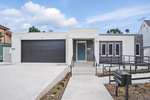 SDA in Penrith 1 Modern single-story house with a flat roof, large black garage door, brick and white facade, front steps, ramp, and mailbox.