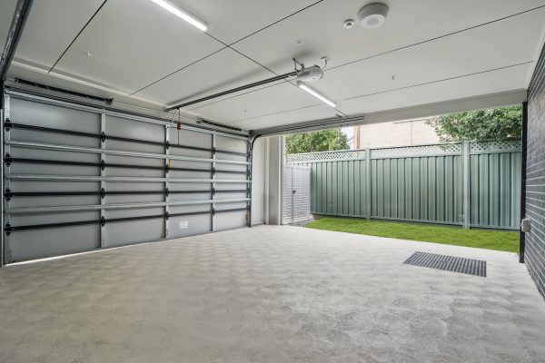 SDA in Penrith 7 Empty garage with an open door, concrete floor, white ceiling, and view of a fenced backyard with green grass.