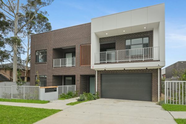 Merrylands SDA 1 Modern two-story house with brick and white facade, featuring balconies and a double garage, surrounded by a white fence and trees.
