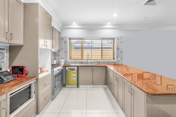 Fairfield 5 Modern kitchen with beige cabinets, orange stone countertops, white tiled floor, stainless steel appliances, and a large window above the sink.