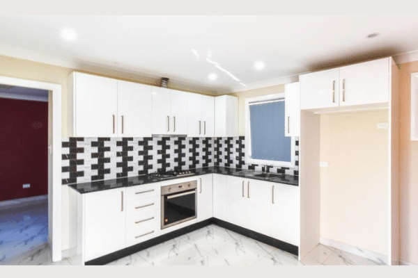 Modern kitchen with white cabinets, black countertop, and black-and-white checkered backsplash. Integrated oven and stove with overhead range hood.