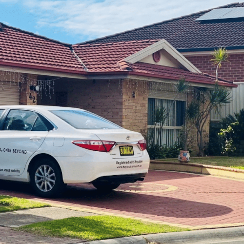 Car with "Beyond Care" branding parked in a residential driveway near a house with solar panels on the roof.