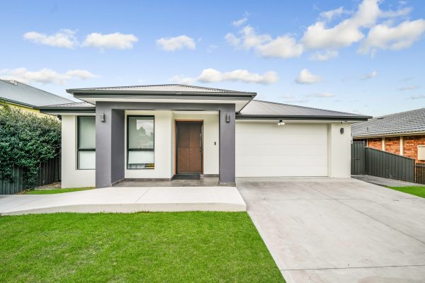Penrith 3 1 Modern single-story house with a flat roof, large garage, front porch, and manicured lawn under a blue sky with scattered clouds.