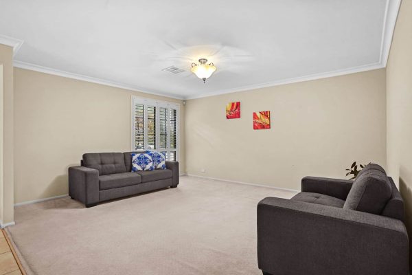 Kellyville 3 A living room with beige walls, two gray sofas, a ceiling light, wall art, shuttered windows, and a small plant in the corner.