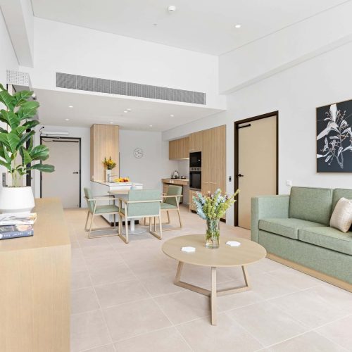 A modern, minimalistic living and dining area with light wood furniture, green sofa, plants, and a wall-mounted artwork in a bright, neutral-toned room.